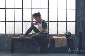 Tired, fit woman resting head on hand sitting in loft gym