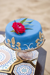 Blue wedding cake on a table and red roses on top in the desert landscape 