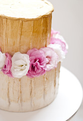Fototapeta na wymiar Gold and white wedding cake and pink flowers around
