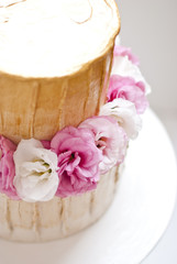 Gold and white wedding cake and pink flowers around