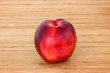 Close-up of a whole ripe nectarine/peach (Prunus persica) on a wooden chopping board.