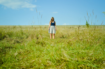 Blonde girl standing in the middle of green field 