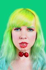 Woman face with two sweet cherry hanging from mouth on green background