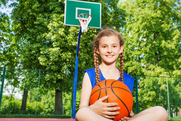 Smiling girl sitting on playground holding ball