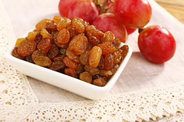 Raisins in bowl with grapes on table close up