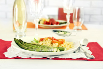 Roasted asparagus and tasty pasta with vegetables on plate on wooden table background