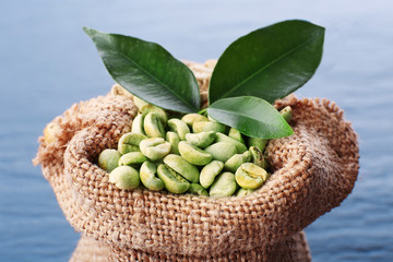 Burlap bag of green coffee beans on wooden table, closeup