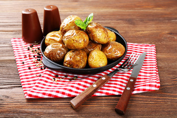 Baked potatoes in pan on wooden table, closeup