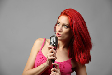 Beautiful young woman with microphone on gray background