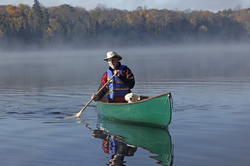 Man Paddling a Canoe with a Small White Dog in the Bow - Ontario, Canada