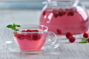 Cup and teapot of raspberry drink with berries on wooden table close up