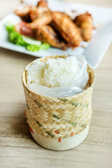 Sticky Rice in bamboo container with fried chicken wings in background