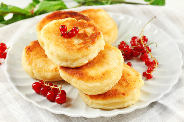 Obraz na płótnie Canvas Fritters of cottage cheese with red currant in plate on table, closeup