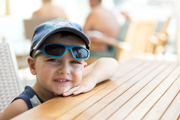 bambino con occhiali e berrettino che ride seduto al tavolo