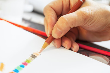 Artist drawing with colour pencil over white paper