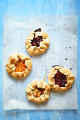 Assorted homemade pies with plums, apricots, sour cherries and peaches on the baking paper on blue painted table