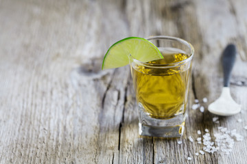 Tequila shot with lime and sea salt on rustic wooden board, selective focus