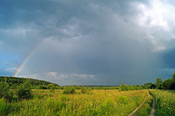 Rainbow and a dirt road in a meadow after rain in summer.