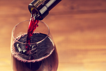 Pouring red wine into the glass against wooden background