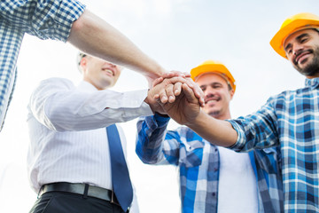 close up of builders in hardhats with hands on top