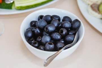 Black Olives in a white Cup on the table. The dish on the table. Serving in the restaurant. Food. Fruits and vegetables. Breakfast, lunch and dinner. Festive table with snacks.