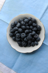 American blueberries (vaccinium corymbosum in small bowl on blue tablecloth