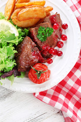 Tasty roasted meat with cranberry sauce and roasted vegetables on plate, on color wooden background