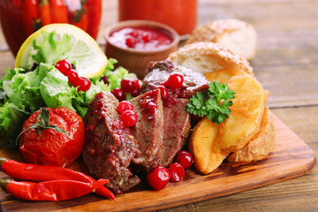 Beef with cranberry sauce, roasted potato slices on cutting board, on wooden background