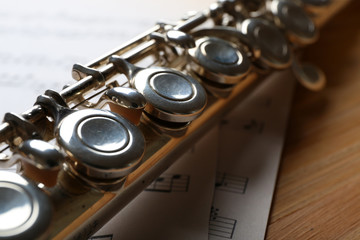 Obraz premium Silver flute with music notes on wooden table close up