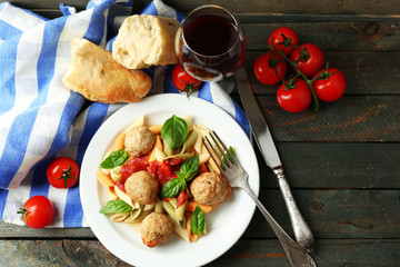 Pasta with meatballs on plate, glass of red wine on wooden  table background