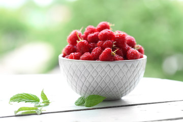 Fresh raspberries in bowl on wooden table on blurred nature background