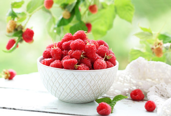 Fresh raspberries in bowl on wooden table on blurred nature background