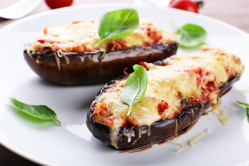 Dish of eggplant with cherry tomatoes and cheese in white plate on wooden table, closeup