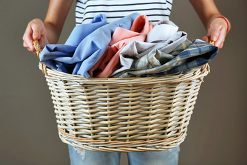 Woman holding basket with clothes on gray background