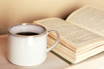 Cup of tea with book on wooden table on light wall background