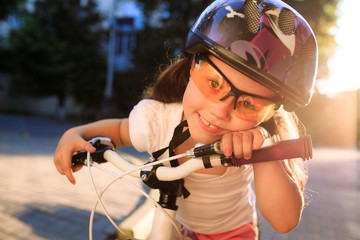 little girl with bicycle in summer park against sunset
