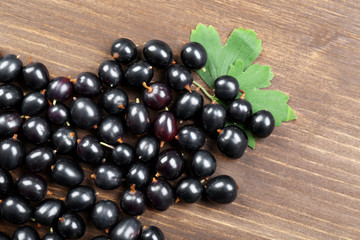 Heap of wild black currant with green leaves on wooden table close up