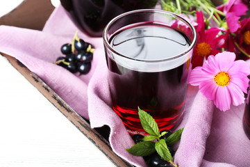 Obraz na płótnie Canvas Glasses of fresh blackcurrant juice on wooden tray with pink napkin and flowers, closeup