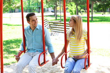 Young pregnant woman with husband on swing outdoors