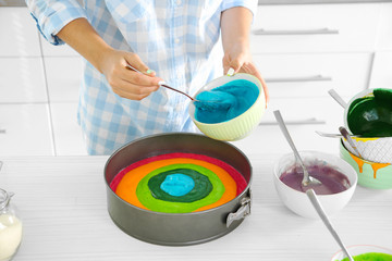 Fototapeta na wymiar Young woman making rainbow cake in kitchen