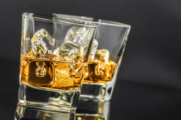 two glasses of whiskey with ice cubes on dark background