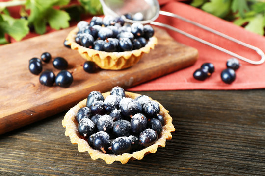 Delicious crispy tarts with black currants on wooden cutting board, closeup