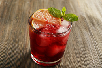 Glass of red currants juice with lemon and ice cubes on wooden table, closeup