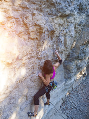 Young woman with rope climbs on the rock.