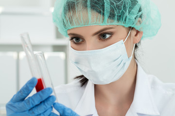female lab worker looking at two flasks with dark red liquid