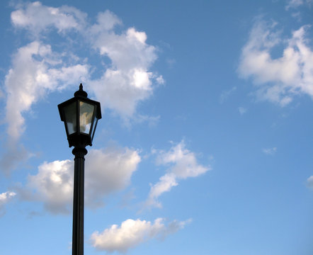 An old-fashioned streetlight against a cloudy, blue, summer sky. Space for text.