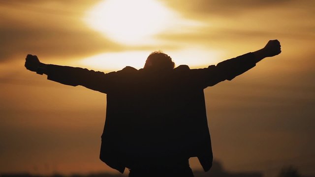 Man raises his hands at sunset
