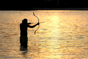 Silhouette archery shoots a bow at a target in sunset sky