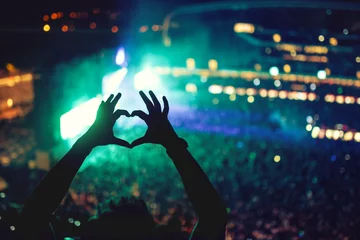 Tuinposter Heart shaped hands at concert, loving the artist and the festival. Music concert with lights and silhouette of a man enjoying the concert © aboutmomentsimages