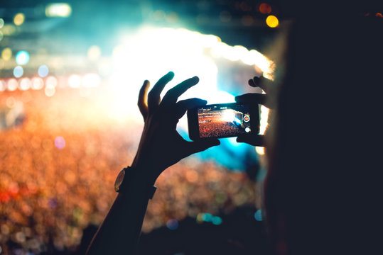Silhouette of a man using smartphone to take a video at a concert. Modern lifestyle with hipster taking pictures and videos at local concert. Main focus on camera and lights.